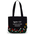 Black tote bag with floral designs and 'Agnes + Cat Wildflower Garden' text on a white background