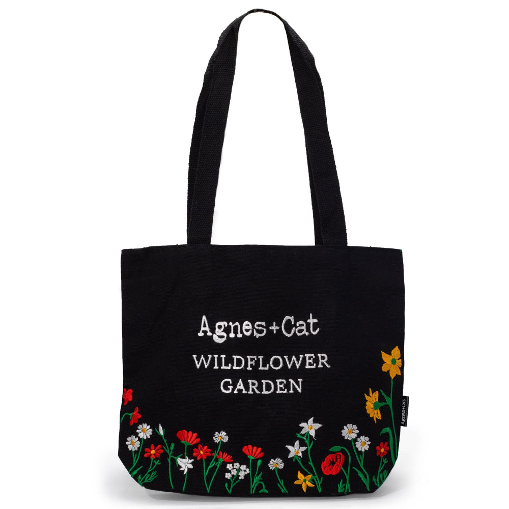 Black tote bag with floral designs and 'Agnes + Cat Wildflower Garden' text on a white background