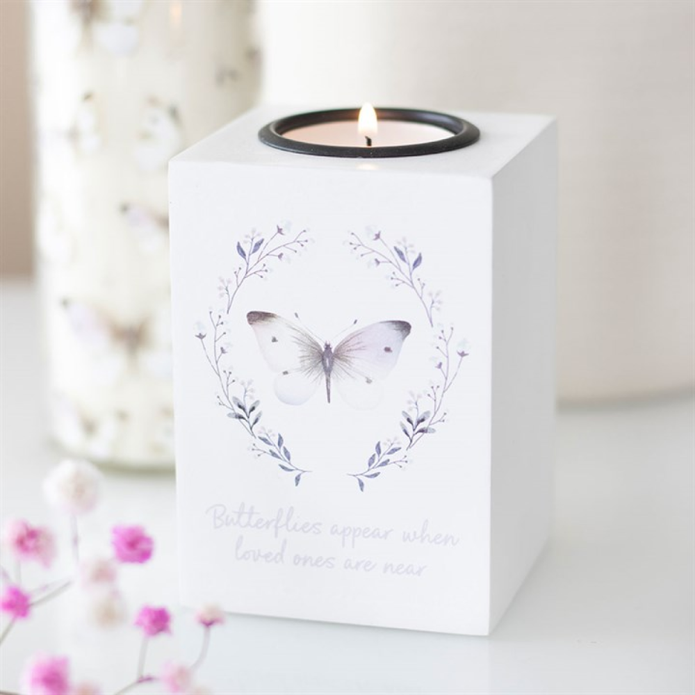 Candle in a white holder with butterfly design and floral text on a light background