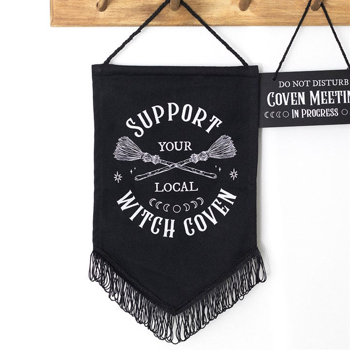 Black banner with white text and broomsticks, hanging on a wooden rod.