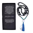 Black and blue beaded necklace with tassel next to a black card with text about the necklace.