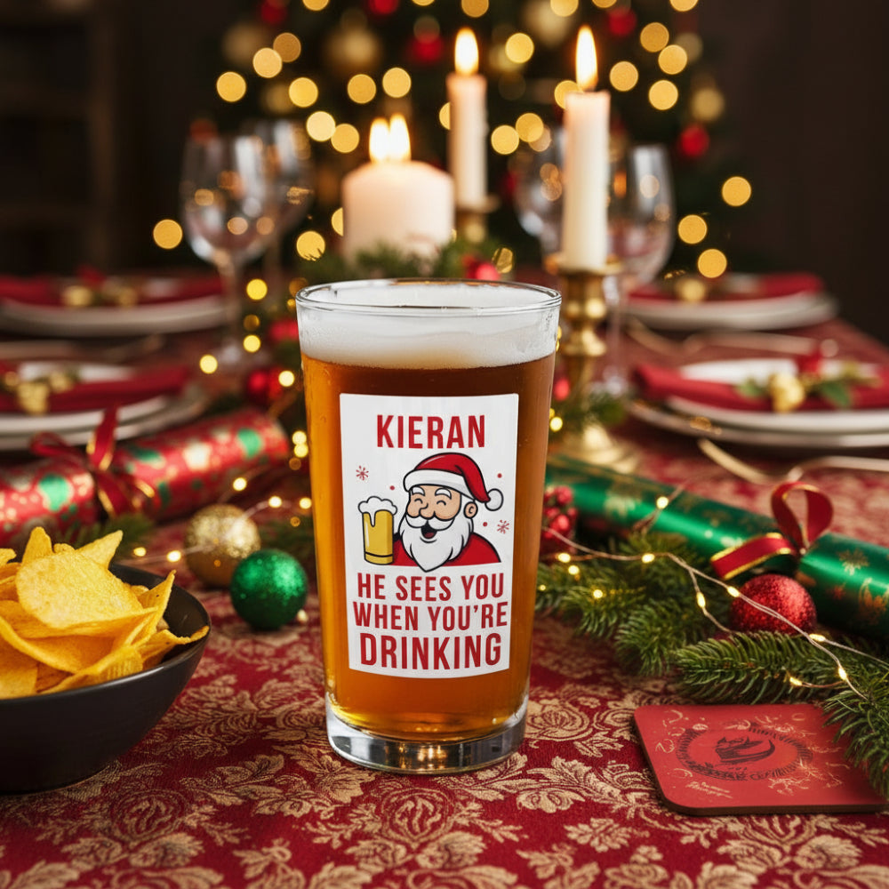 Beer glass with a Santa Claus label on a wooden table with chips and a coaster.