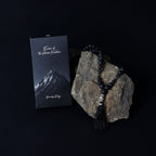 Black beaded necklace with tassel on a rock next to a mountain-themed card on a black background