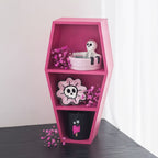Pink coffin-shaped shelf with decorative items on a plain background