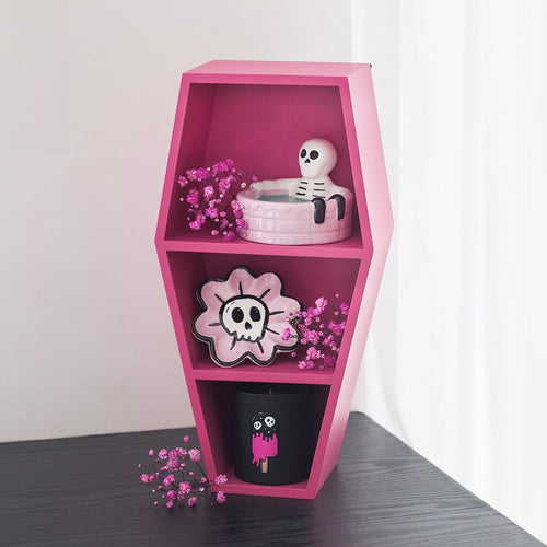 Pink coffin-shaped shelf with decorative items on a plain background