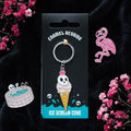 Enamel keyring with ice cream cone and skull design on a black card, surrounded by pink flowers.