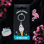 Enamel keyring with ice cream cone and skull design on a black card, surrounded by pink flowers.