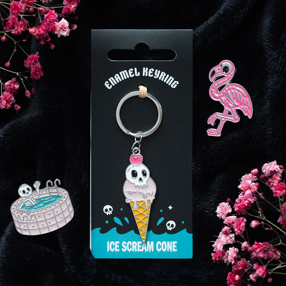 Enamel keyring with ice cream cone and skull design on a black card, surrounded by pink flowers.