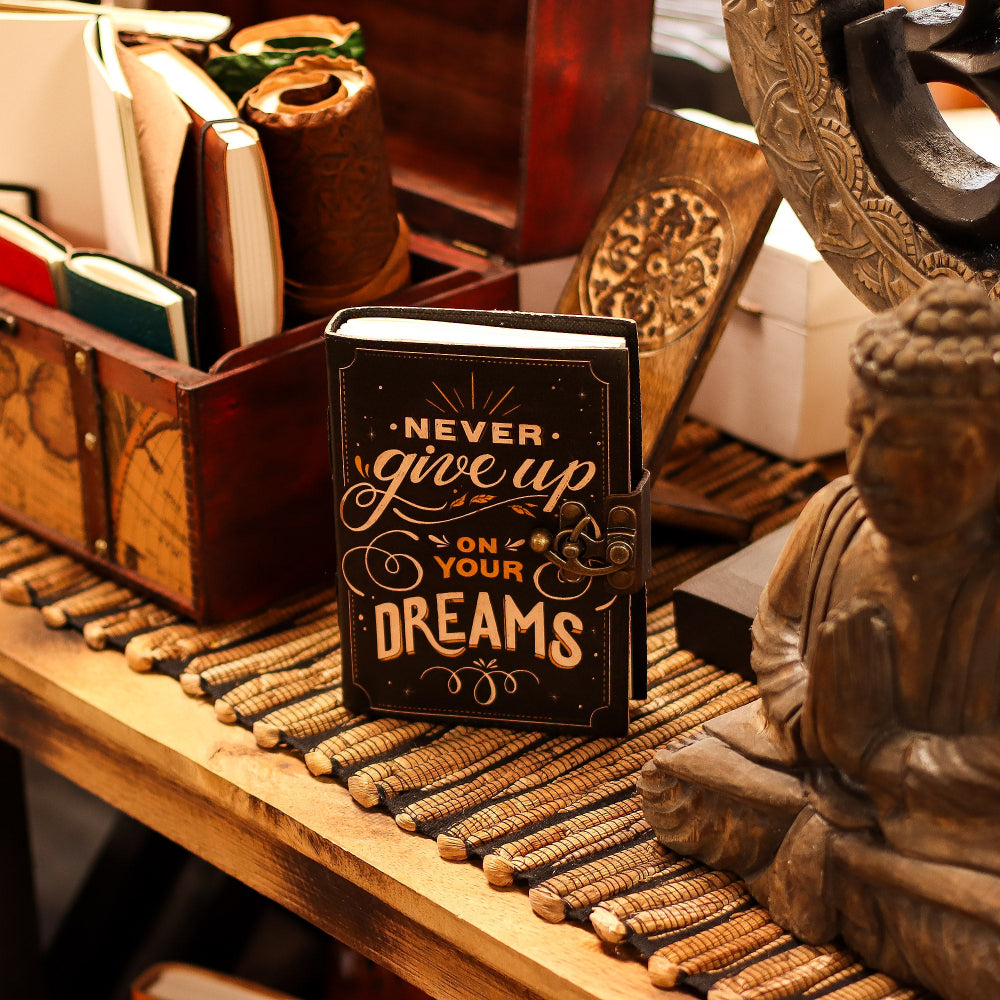 Decorative book with 'Never give up on your dreams' quote on a wooden surface with a Buddha statue.