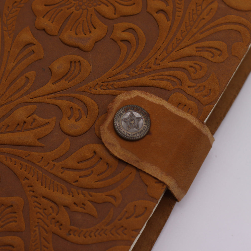 Close-up of a brown leather belt with intricate floral embossing and a metal buckle.