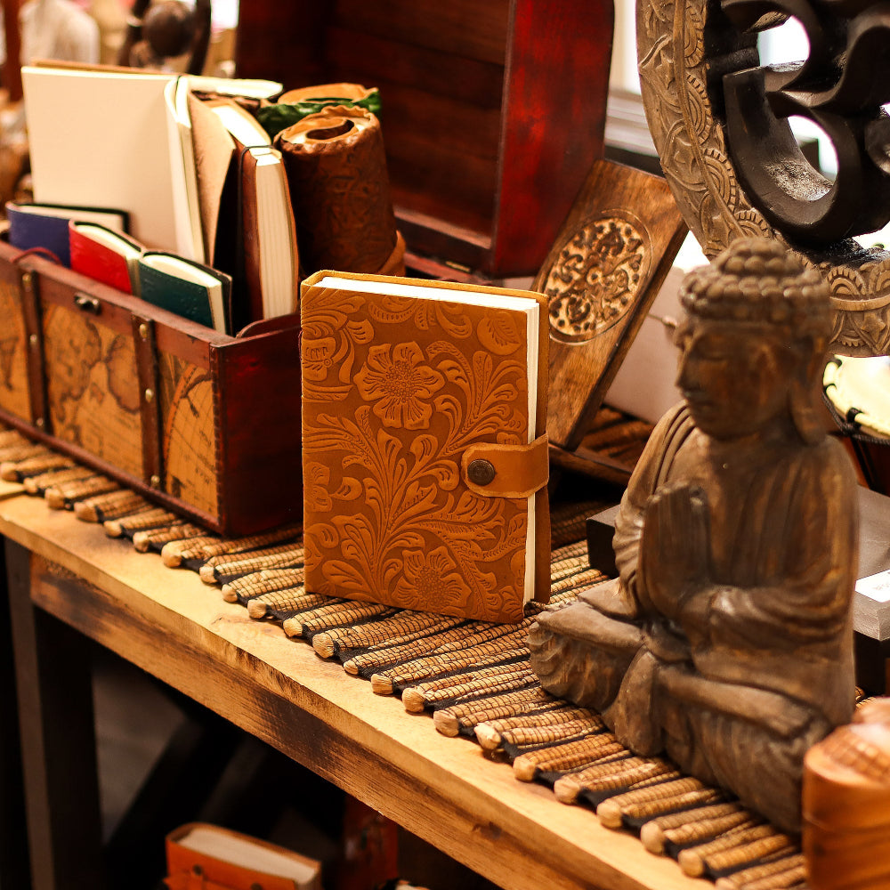 Wooden notebook with intricate design on a wooden surface with a Buddha statue and other items.
