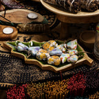 Colorful stones on a wooden tray with candles and herbs on a patterned surface