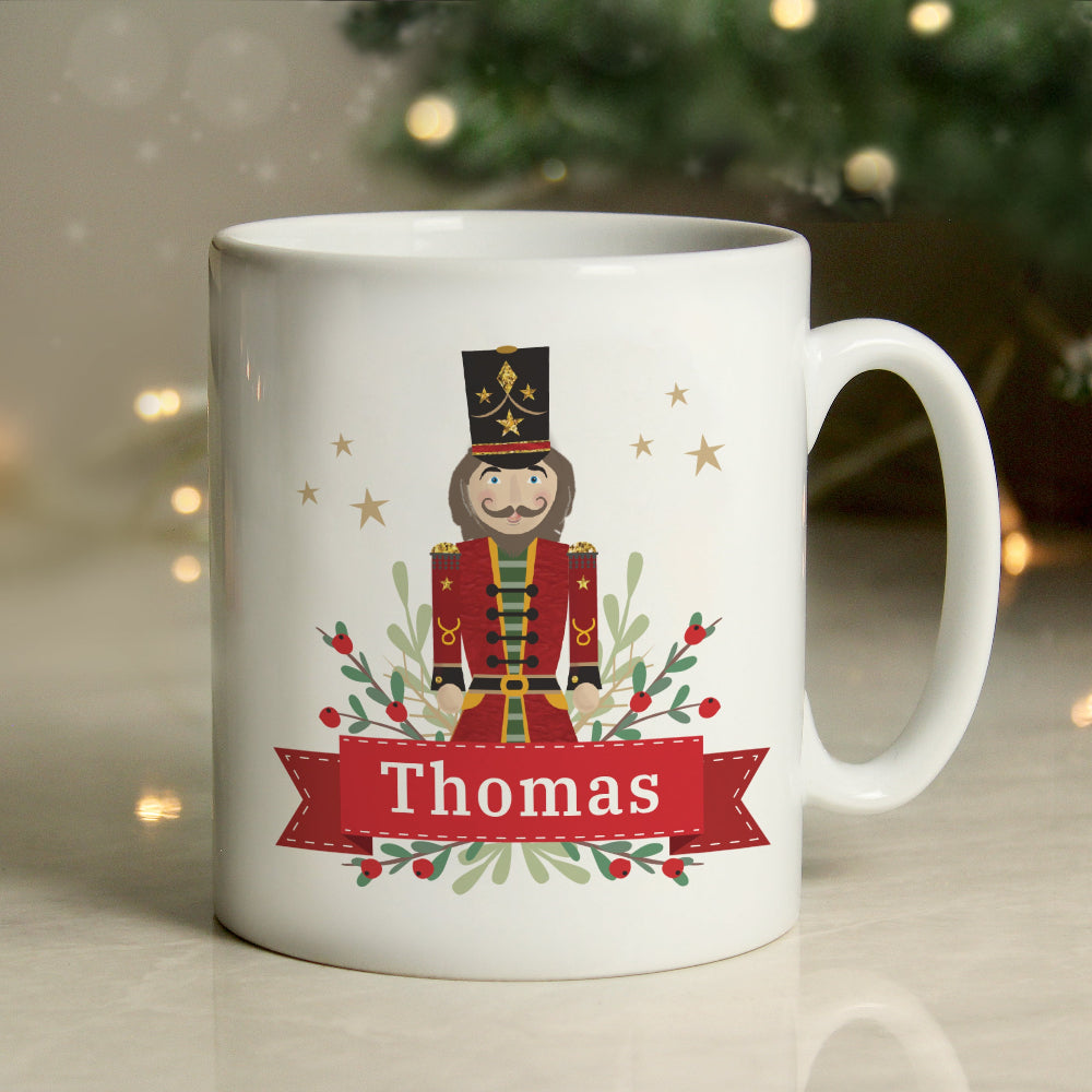 White mug with a Christmas-themed design of a nutcracker and the name 'Thomas', against a blurred festive background.