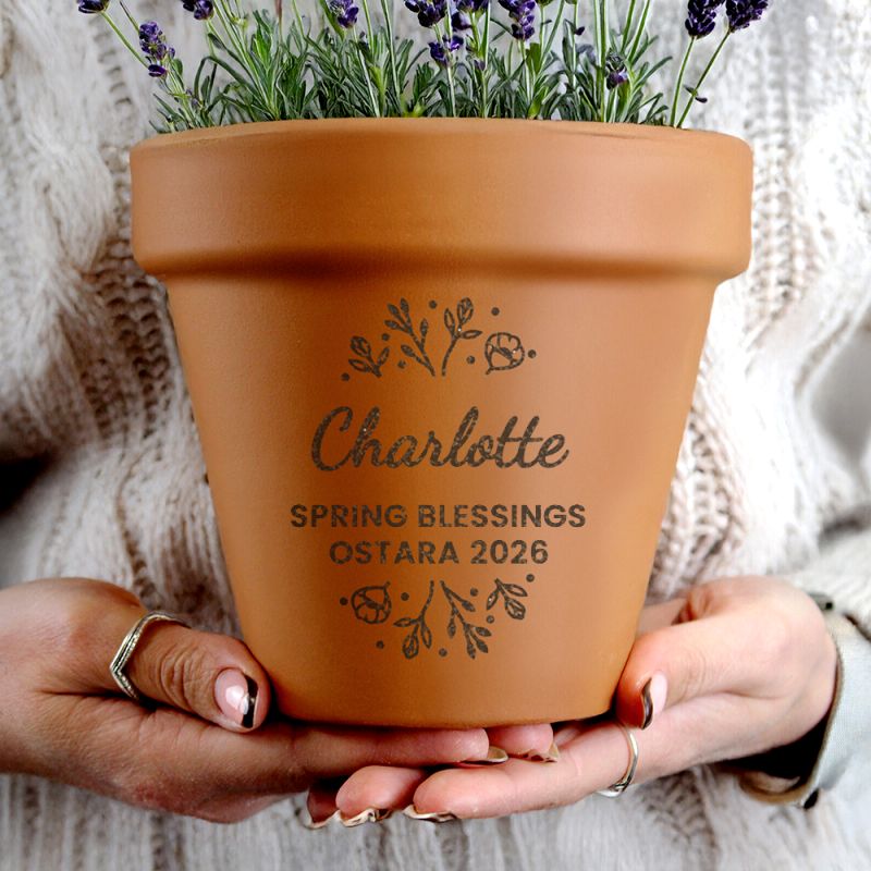 Terracotta pot with engraved text held by hands against a textured background