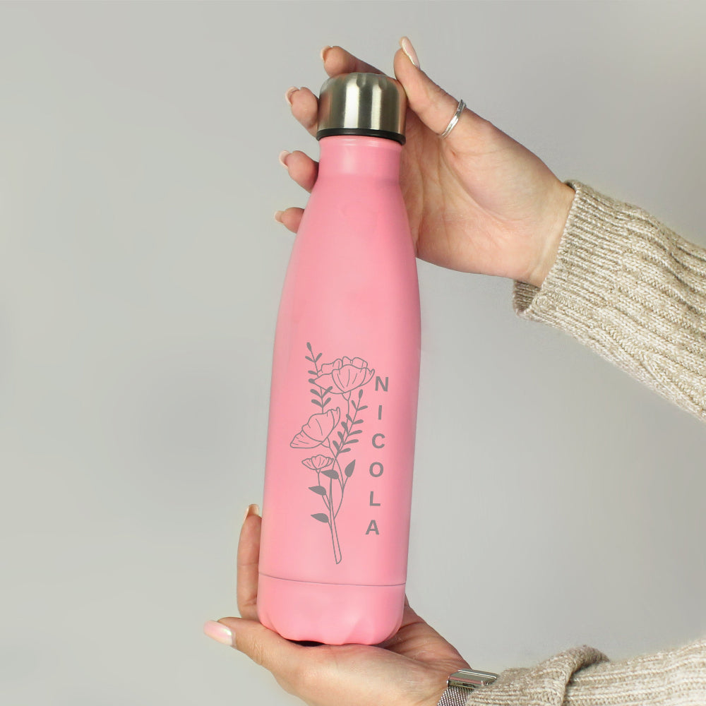 Pink water bottle with floral design and 'Nicola' text held by a person against a gray background