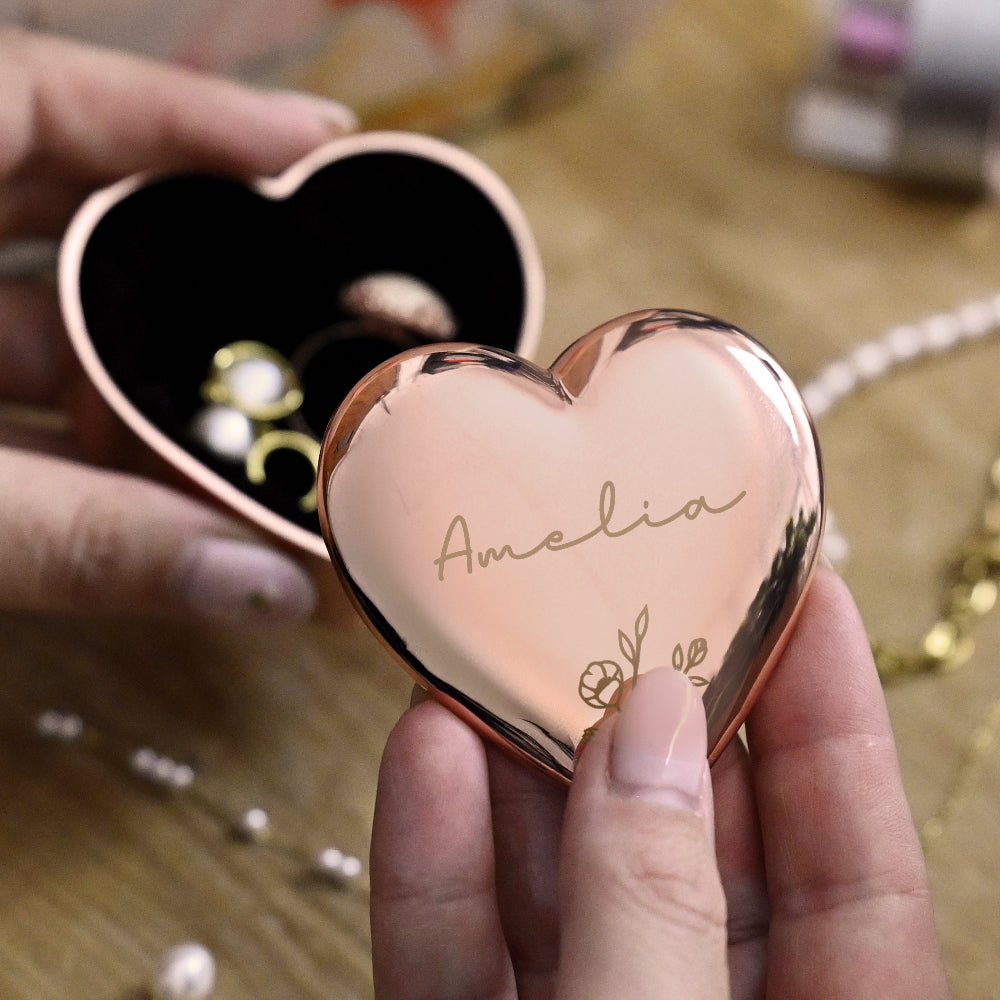 Heart-shaped rose gold compact mirror with 'Amelia' engraved, held by a hand.