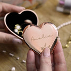 Heart-shaped rose gold compact mirror with 'Amelia' engraved, held by a hand.