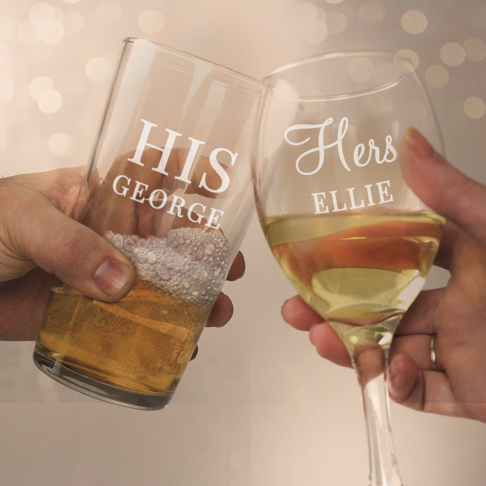 Two wine glasses, one labeled 'HIS GEORGE' and the other 'HERS ELLIE', being held together.