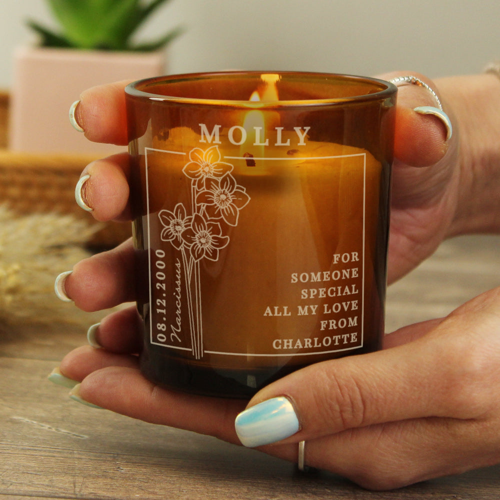 Person holding a personalized candle with engraved text and floral design.