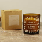 Personalized autumn-themed candle with decorative text and pumpkins, next to its cardboard box on a wooden surface.