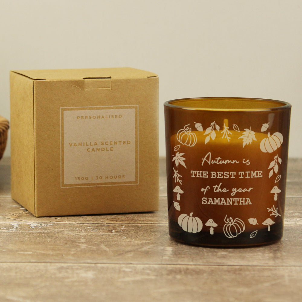 Personalized autumn-themed candle with decorative text and pumpkins, next to its cardboard box on a wooden surface.