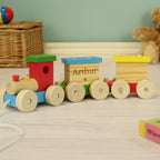Wooden toy train with colorful cars on a wooden floor, featuring a teddy bear and wicker basket in the background.