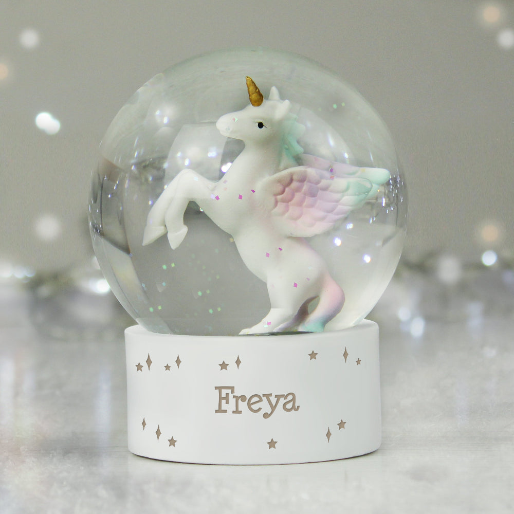 Unicorn figurine inside a snow globe with 'Freya' on a stand against a blurred background