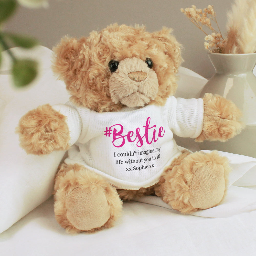 Teddy bear wearing a '#Bestie' shirt with a message on a white surface.