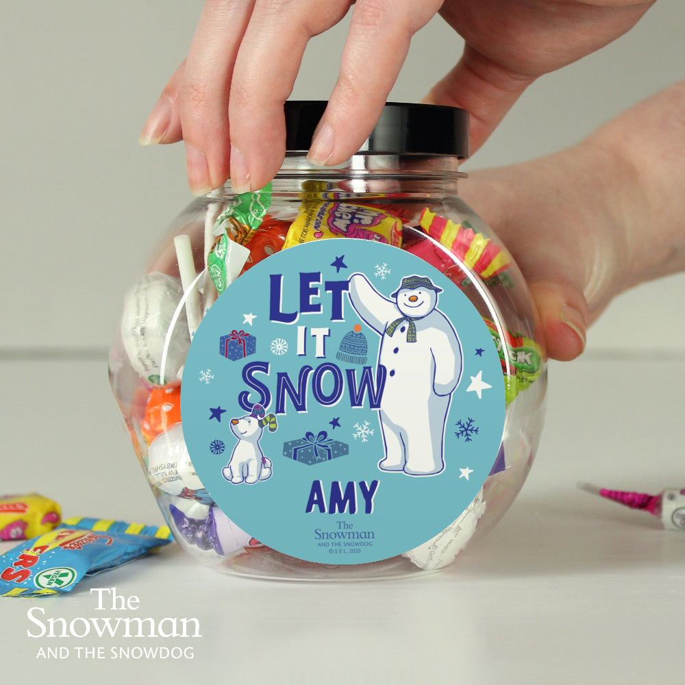 Clear jar filled with colorful candies and a 'Let It Snow' label featuring a snowman character, held by a hand.