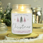 Candle jar with a Christmas-themed label on a wooden surface with decorative lights in the background
