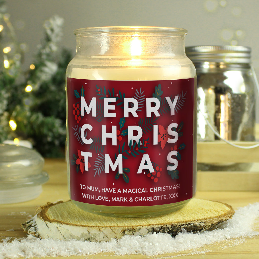 Candle jar with a 'Merry Christmas' label on a wooden surface with a festive background.