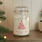 Glass jar candle with Christmas tree design and 'Christmas Wishes Scarlett' text on a wooden surface.