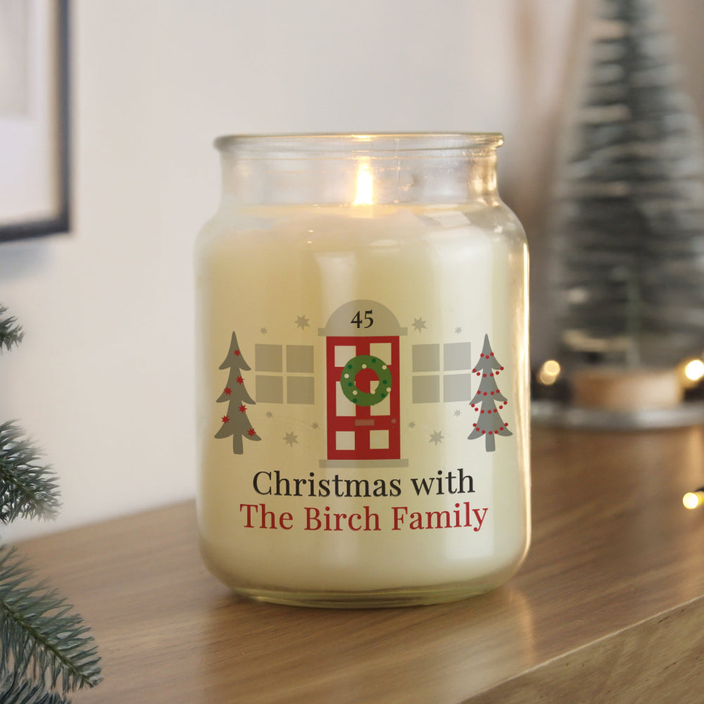 Candle jar with Christmas-themed label on a wooden surface, surrounded by festive decorations.