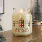 Candle jar with Christmas-themed label on a wooden surface, surrounded by festive decorations.