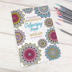 Personalized mandala coloring book with colored pencils on a wooden surface