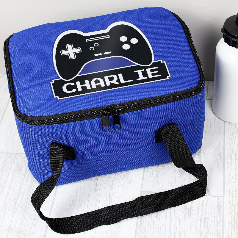 Blue insulated lunch bag with a gaming controller design and the name 'Charlie' on a light wooden surface.