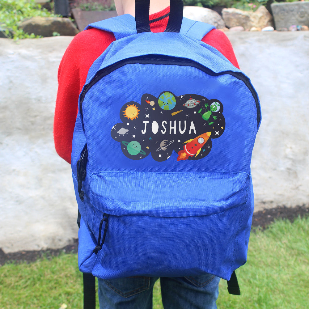 Blue backpack with space-themed design and 'Joshua' text, worn by a person outdoors.