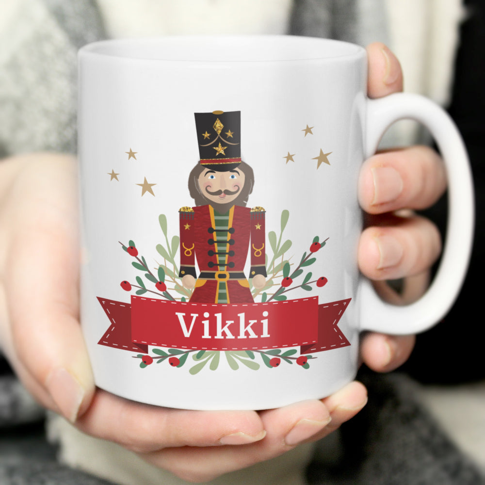 White mug with a Nutcracker design and the name 'Vikki' held by a person.