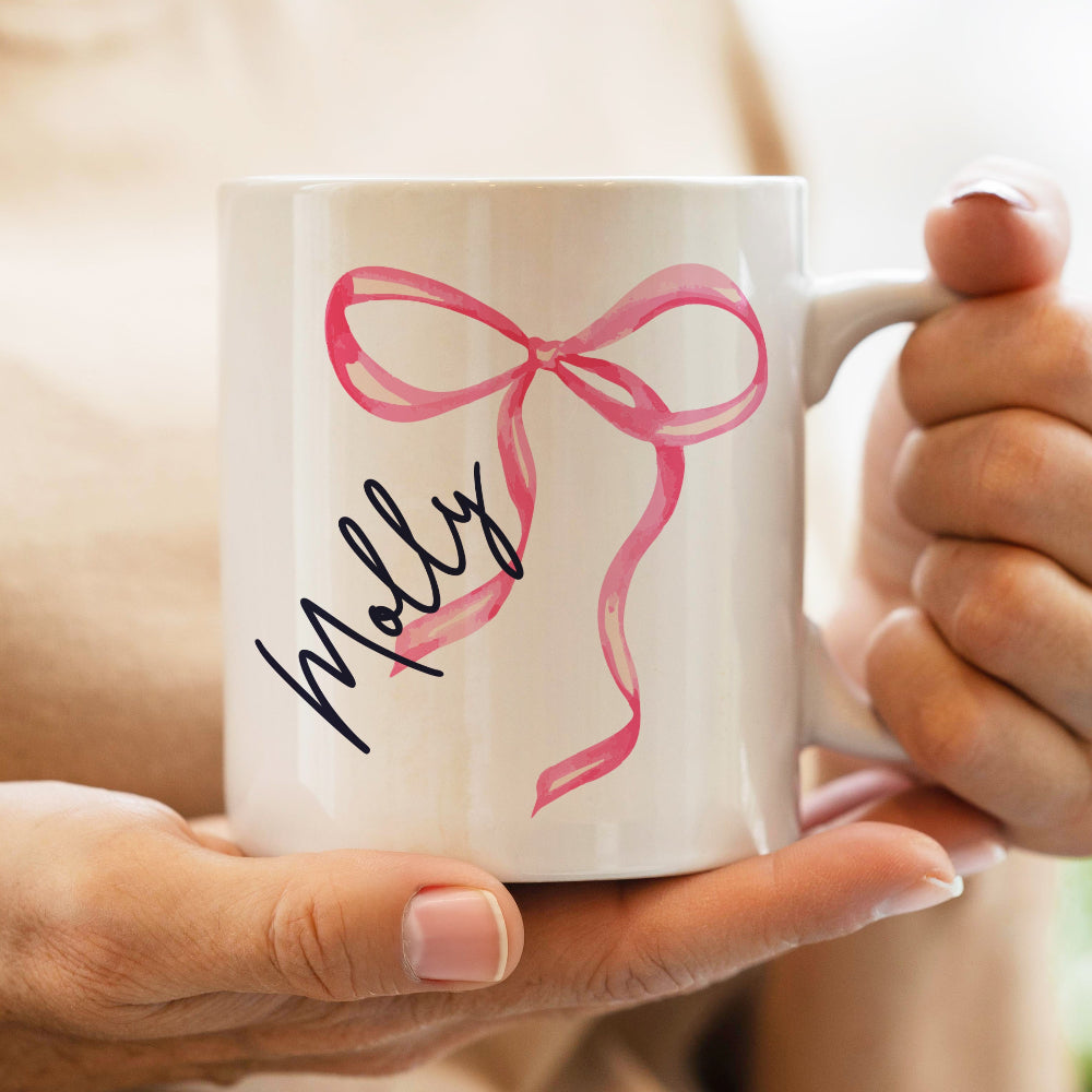 White mug with pink bow and 'Molly' text held by a person