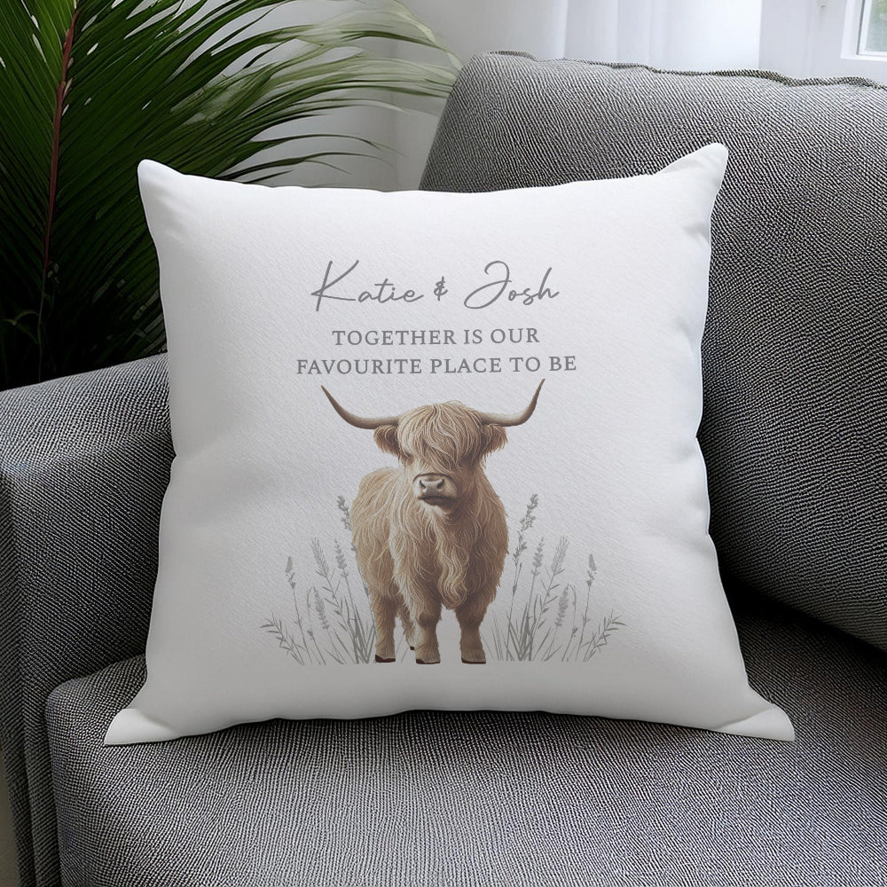 Decorative pillow with a highland cow illustration and text on a gray couch.