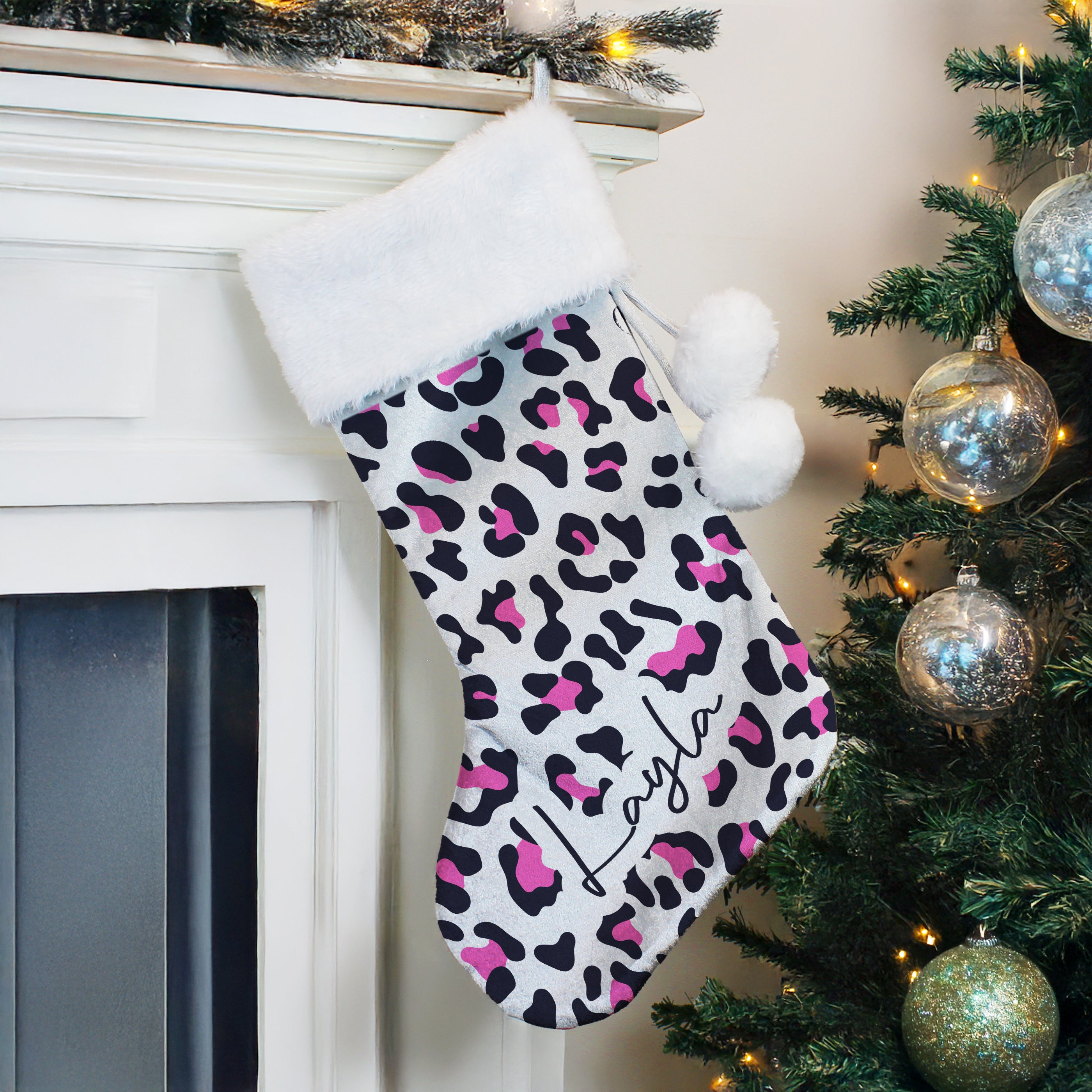 Christmas stocking with pink and black pattern hanging on a fireplace next to a decorated tree.