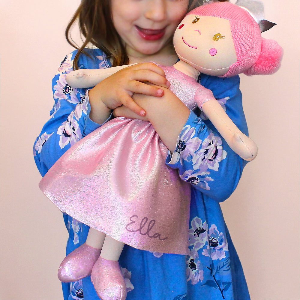 Child holding a doll with a pink dress labeled 'Ella' against a plain background