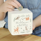 Child's hand placing a coin into a white piggy bank with animal illustrations and text.