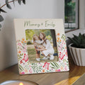 Floral photo frame with a picture of two women hugging, placed on a surface with plants in the background.