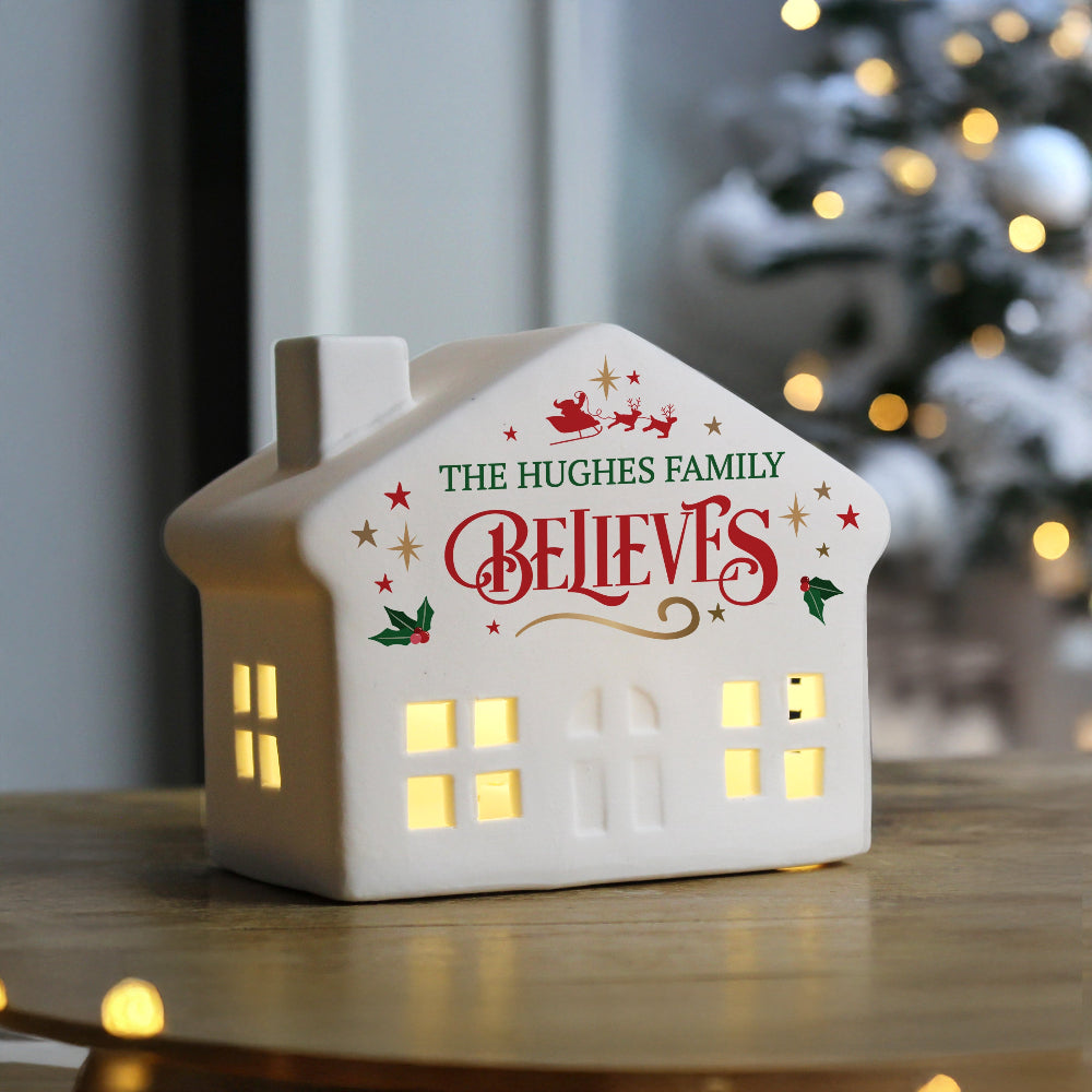 Decorative house-shaped light with 'The Hughes Family Believes' text, glowing softly on a wooden surface.