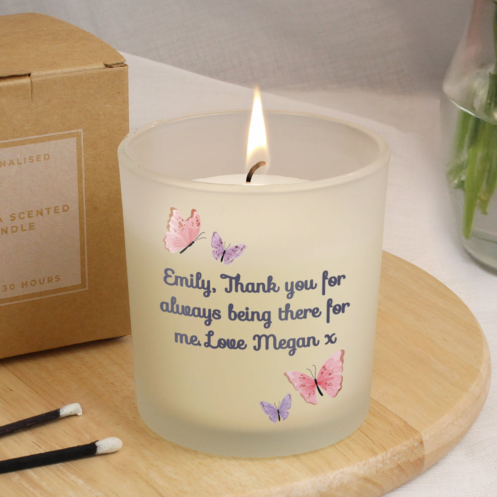 Candle with butterflies and text on a wooden coaster, next to a cardboard box and matches.
