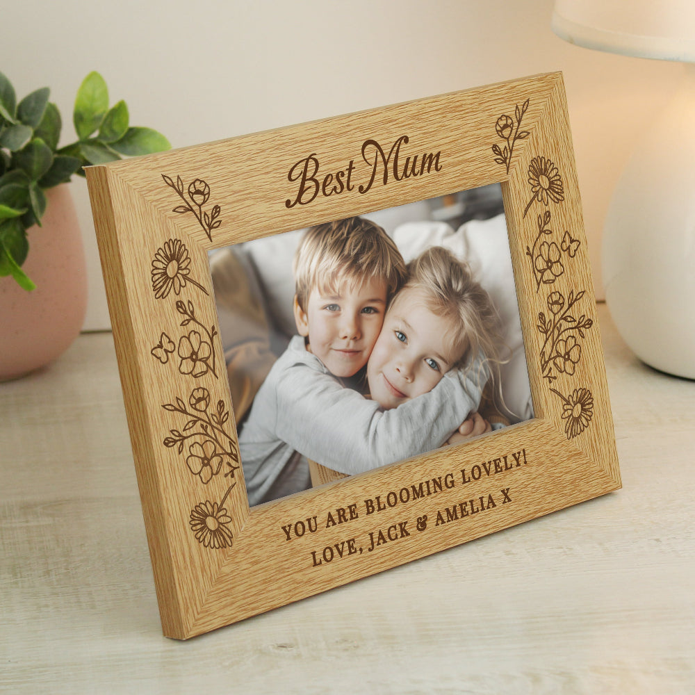 Wooden photo frame with engraved message and photo of two children, placed on a surface with a plant and candle in the background.