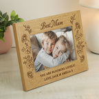 Wooden photo frame with engraved message and photo of two children, placed on a surface with a plant and candle in the background.