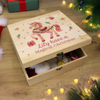 Wooden Christmas box with unicorn design and text 'Lily have a Magical Christmas' on a wooden surface with festive decorations.