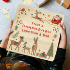 Person holding a Christmas Eve box with festive illustrations and text.